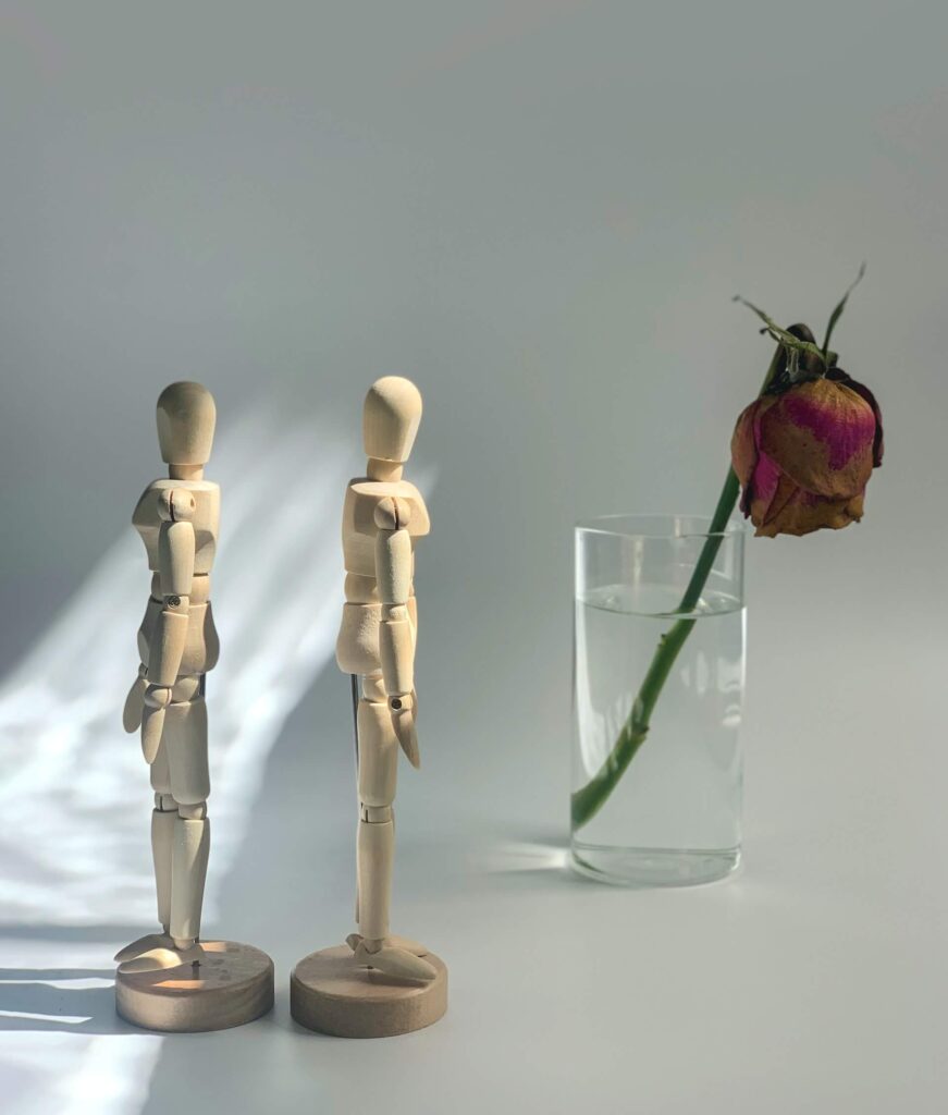 Wooden human toy figures and a dying rose in a glass of water