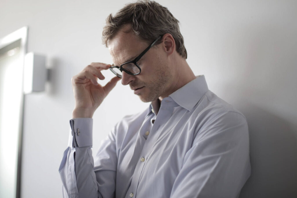 A man holding his eyeglasses while looking down and thinking